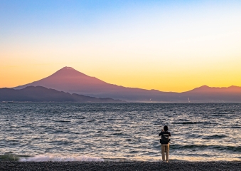三保海岸から見る明け方の富士山。水色、白色、橙色にグラデーションがかかった空と朧げな富士山のシルエットが幻想的。