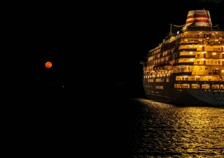 11月20日、真っ暗な夜の海に浮かぶ船体、暖かなオレンジ色にライトアップさている。空に浮かぶ丸い月も似た色をしている。